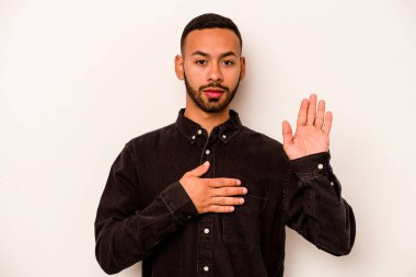 Genç İspanyol bir adam beyaz arka planda izole edilmiş yemin ediyor, elini göğsüne koyuyor..