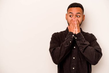 Genç İspanyol bir adam beyaz arka planda izole edilmiş. Düşünceli bir şekilde bir fotokopi odasına bakıyor. Ağzını eliyle kapatıyor..