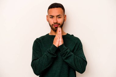Latin kökenli genç bir adam beyaz arka planda izole edilmiş dua ediyor, bağlılık gösteriyor, dindar biri ilahi ilham arıyor..