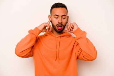 Beyaz arka planda izole edilmiş, kulakları parmaklarla kaplayan, stresli ve çaresiz genç bir İspanyol..