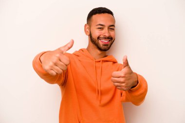 Beyaz arka planda izole edilmiş genç bir İspanyol. Baş parmağını kaldırıyor, gülümsüyor ve kendinden emin..