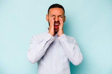 Genç İspanyol adam mavi arka planda izole edilmiş, heyecanlı bir şekilde bağırıyor..