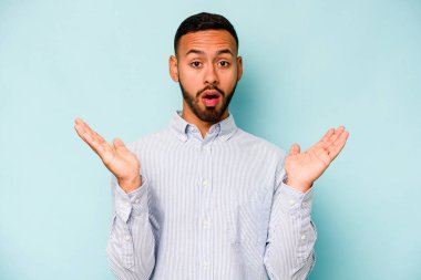 Genç İspanyol adam mavi arka planda izole edildi. Şaşırdı ve şok oldu..