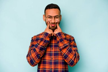 Latin kökenli genç bir adam mavi arka planda iki seçenek arasında kuşkulanıyor..