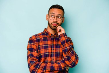 Genç İspanyol adam mavi arka planda izole edilmiş düşünüyor, bakıyor, yansıtıyor, düşünüyor, hayal kuruyor..