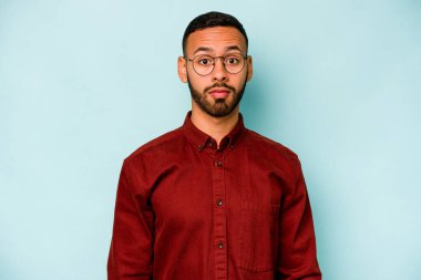 Genç İspanyol adam mavi arka planda izole edilmiş üzgün, ciddi yüz, mutsuz ve hoşnutsuz hissediyor.