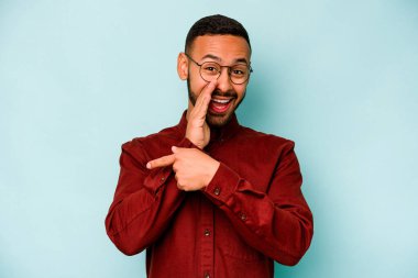 Genç İspanyol bir adam mavi arka planda izole edilmiş. Dedikodu yapıyor, bir şeyleri bildiriyor..