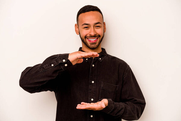 Young hispanic man isolated on white background holding something with both hands, product presentation.