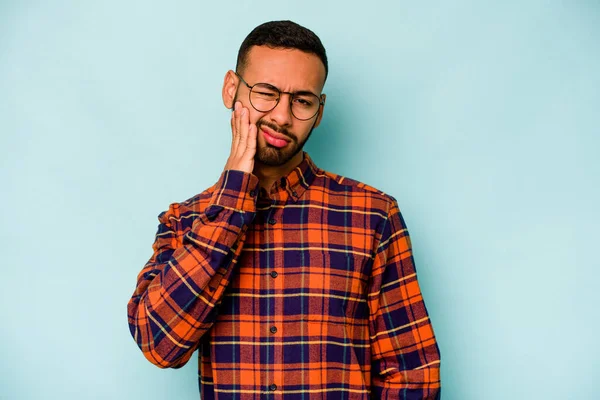 Genç İspanyol bir adam mavi arka planda izole edilmiş güçlü bir diş ağrısı, azıdişi ağrısı var..