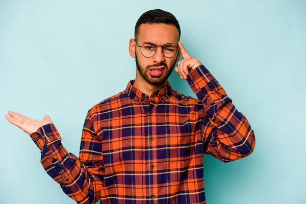 Genç İspanyol bir adam mavi arka planda izole edilmiş ve elinde bir ürün tutuyor..