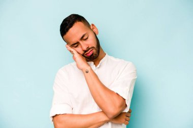 Genç İspanyol adam mavi arka planda izole edilmiş. Tekrarlanan bir görevden yorulmuş..