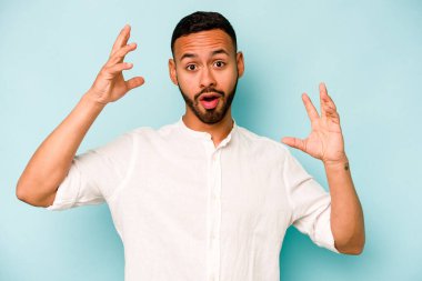 Latin kökenli genç bir adam mavi arka planda zaferi ya da başarıyı kutlarken şaşırmış ve şok olmuştu..