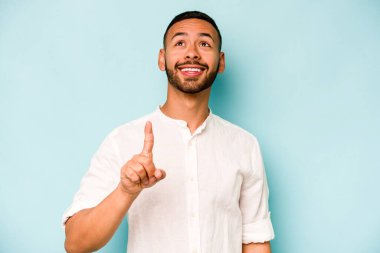 Mavi arka planda izole edilmiş genç İspanyol bir adam iki parmağı da boş bir alan gösteriyor..