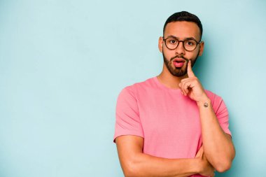 Genç İspanyol adam mavi arka planda izole edilmiş şüpheli ve şüpheci bir ifadeyle yana bakıyor..