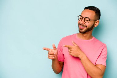 Genç İspanyol adam mavi arka planda izole edilmiş başparmak uzakta, gülüyor ve kaygısız.
