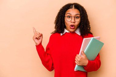 Genç Afrikalı Amerikalı kadın. Bej arka planda izole edilmiş. Yan tarafı işaret ediyor.