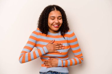 Beyaz arka planda izole edilmiş genç Afrikalı Amerikalı kadın mutlu bir şekilde gülüyor ve ellerini karnının üstünde tutarak eğleniyor..