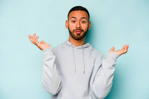 Joven Hombre Hispano Aislado Sobre Fondo Azul Dudando Encogiéndose Hombros — Foto de Stock