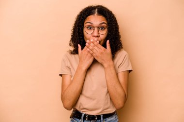 Genç Afrikalı Amerikalı kadın bej arka planda izole edilmiş şok geçirmiş, ağzı ellerle kaplanmış, yeni bir şey keşfetmeye hevesli..