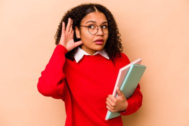 Genç Afrikalı Amerikalı kadın, bej arka planda izole edilmiş bir şekilde bir dedikoduyu dinlemeye çalışıyor..