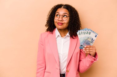 Genç Afrikalı Amerikalı iş kadını bej arka planda izole edilmiş banknotları tutuyor hedeflere ve amaçlara ulaşma hayali kuruyor.