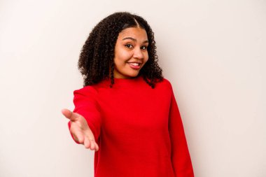 Beyaz arka planda izole edilmiş genç Afrikalı Amerikalı kadın selamlaşma jesti olarak kameraya uzanıyor..