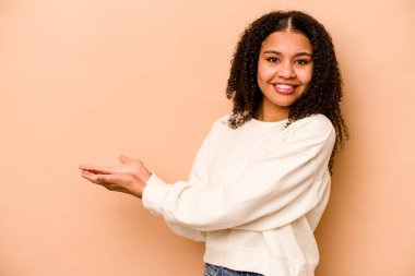 Genç Afrikalı Amerikalı kadın bej arka planda izole edilmiş. Elinde palmiye ağacında bir kopya alanı var..