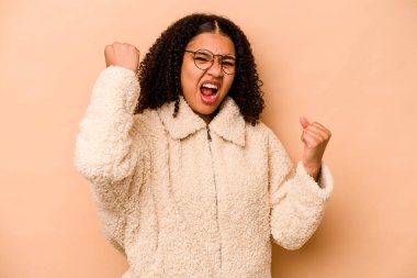 Genç Afrikalı Amerikalı kadın bej arka planda izole edilmiş tasasız ve heyecanlı bir şekilde tezahürat yapıyor. Zafer konsepti.