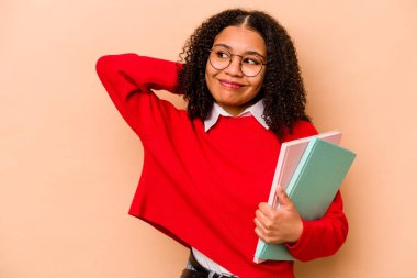 Genç Afrikalı Afrikalı Amerikalı kadın bej arka planda izole edilmiş kafasının arkasına dokunuyor, düşünüyor ve bir seçim yapıyor..