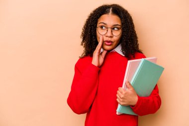 Genç Afrikalı Amerikalı kadın, bej arka planda izole edilmiş bir şekilde gizli bir fren haberi veriyor ve bir kenara bakıyor.