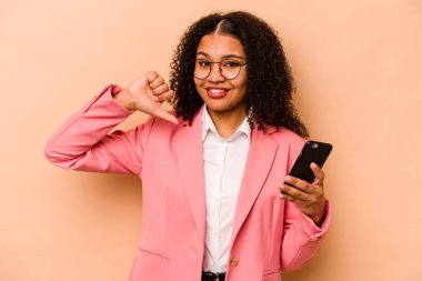 Bej arka planda izole edilmiş cep telefonu tutan genç Afrikalı Amerikalı kadın gururlu ve kendinden emin hissediyor..