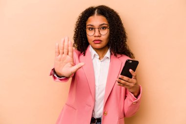 Elinde bej arka planda izole edilmiş cep telefonu tutan genç Afrikalı Amerikalı kadın uzanmış elinde dur işareti ile duruyor..
