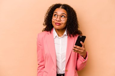 Elinde cep telefonu olan genç Afrikalı bir kadın bej arka planda izole edilmiş hedeflere ve amaçlara ulaşma hayali kuruyor.