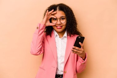 Elinde cep telefonu olan genç Afrikalı bir kadın bej arka planda izole edilmiş..