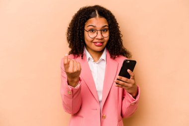 Elinde cep telefonu olan genç Afrikalı bir kadın bej arka planda izole bir şekilde seni işaret ediyor. Sanki seni davet ediyormuş gibi..