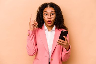 Elinde cep telefonu olan genç Afrikalı bir kadın bej arka planda izole edilmiş. Harika bir fikir, yaratıcılık kavramı var..