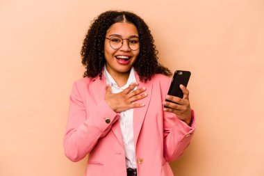 Bej arka planda cep telefonu tutan genç Afrikalı Amerikalı kadın elini göğsünde tutarak kahkahalar atıyor..