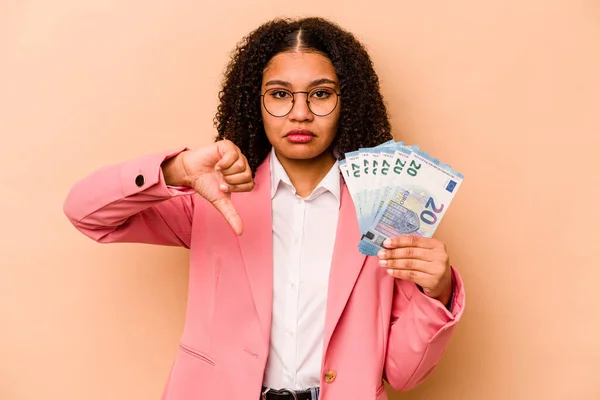 若いアフリカ系アメリカ人のビジネス女性がベージュの背景に孤立した銀行券を保持ジェスチャー 親指ダウン嫌いな示しています 意見の相違 — ストック写真
