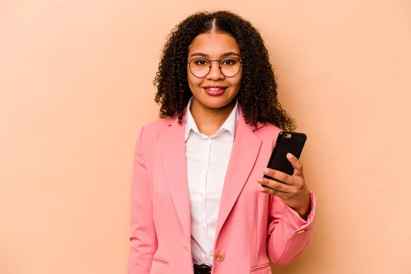 Young African American woman holding mobile phone isolated on beige background happy, smiling and cheerful.