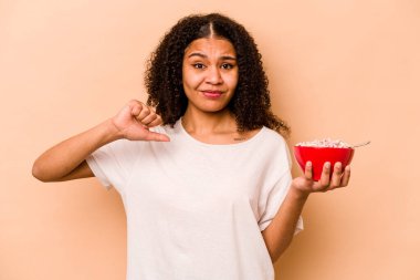 Young African American woman holding a bowl of cereals isolated on beige background feels proud and self confident, example to follow.