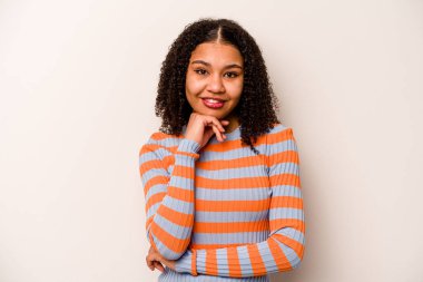 Beyaz arka planda izole edilmiş genç Afrikalı Amerikalı kadın mutlu ve kendinden emin gülümsüyor, elleriyle çenesine dokunuyor..