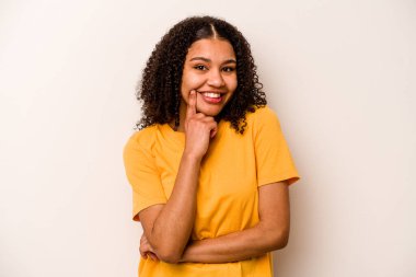Beyaz arka planda izole edilmiş genç Afrikalı Amerikalı kadın mutlu ve kendinden emin gülümsüyor, elleriyle çenesine dokunuyor..