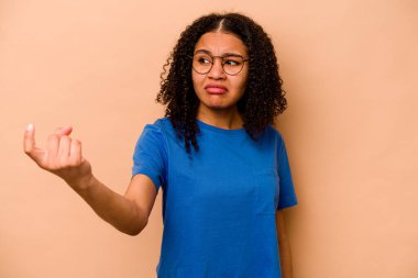 Genç Afro-Amerikalı kadın bej arka planda izole edilmiş. Sanki seni davet ediyormuş gibi parmağıyla işaret ediyor..