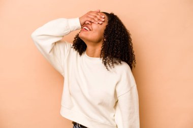 Bej arka planda izole edilmiş genç Afrikalı Amerikalı kadın ellerini başının üstünde tutarak neşe içinde gülüyor. Mutluluk kavramı.