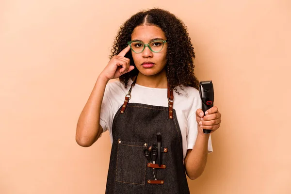 Young African American hairdresser woman isolated on beige background pointing temple with finger, thinking, focused on a task.
