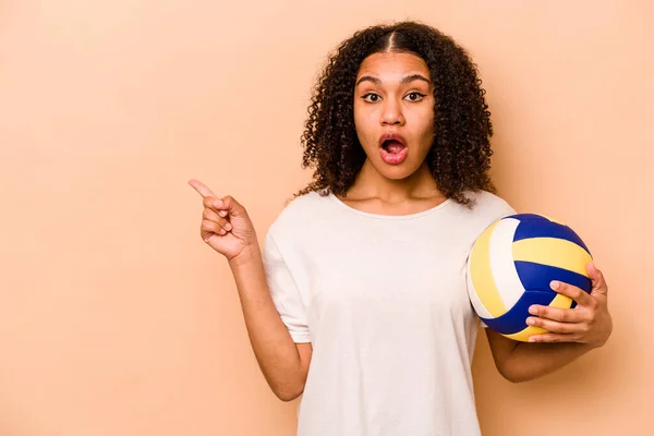 Молода Афроамериканська Жінка Грає Волейбол Ізольований Бежевому Фоні Вказує Бік — стокове фото