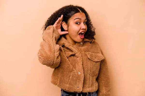 Genç Afrikalı Amerikalı kadın bej arka planda izole edilmiş bir şekilde bir dedikoduyu dinlemeye çalışıyor..