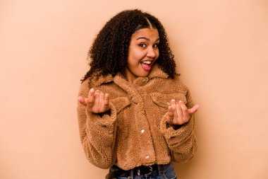 Genç Afro-Amerikalı kadın bej arka planda izole edilmiş. Sanki seni davet ediyormuş gibi parmağıyla işaret ediyor..