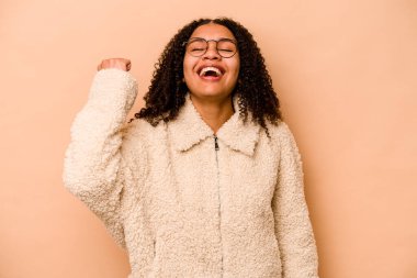 Genç Afrikalı Amerikalı kadın bej arka planda izole edilmiş zafer, tutku ve coşkuyu kutluyor, mutlu bir ifade..