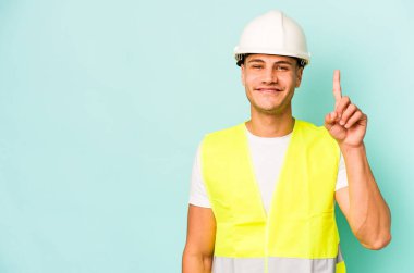 Genç işçi beyaz adam mavi arka planda izole edildi. Bir numarayı parmağıyla gösteriyor..